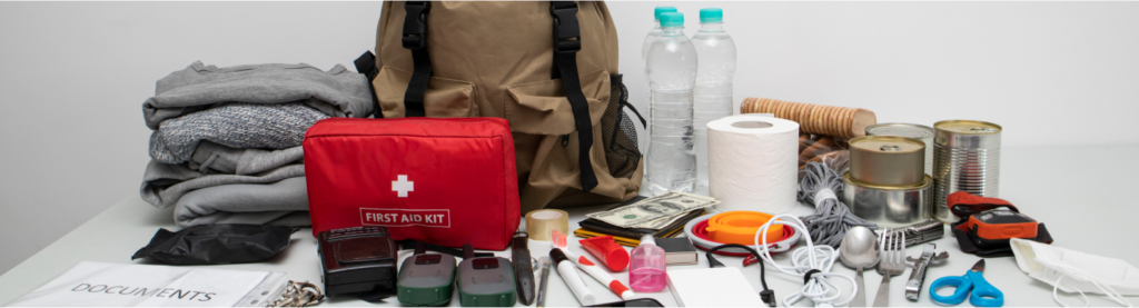 Elements that go into an emergency go bag, including a first aid kit, blankets, cash, cutllery, toilet paper, canned food and scissors.