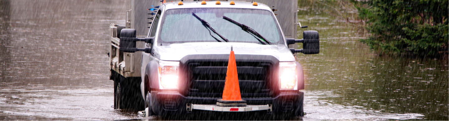 Utility truck driving through a rain storm with flooding on the street.